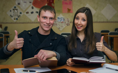 Obraz premium Pass exam. Lesson. Lecture. Two students in classroom hold textbooks in one hand and the other hand show thumbs up.