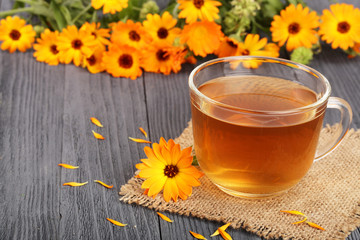 Calendula tea with fresh flowers on black wooden background