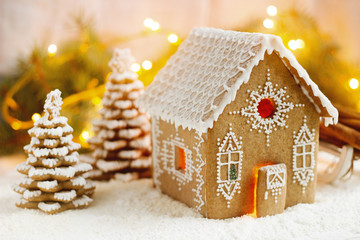 Gingerbread house and Christmas trees on a luminous background. Bokeh effect.