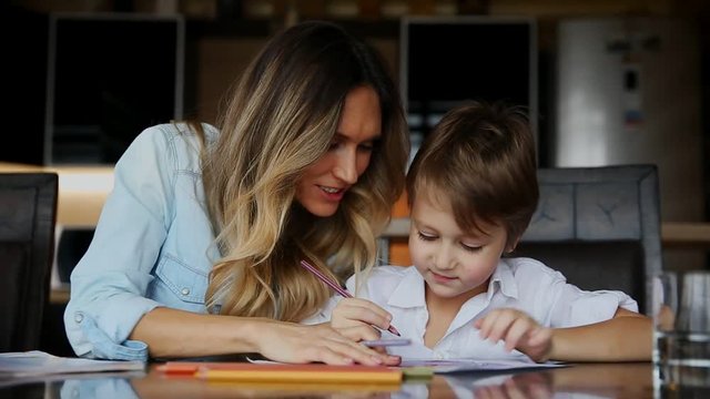 Beautiful mom helps her son to paint with colored pencils image. Helping to develop a child's imagination.