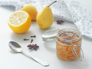 Jam with pear and poppy seeds in a glass jar upon white wooden table with rustic napkin. Selective focus on the jar.
