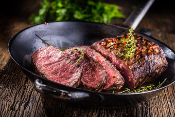 Beef steak. Juicy medium Rib Eye steak slices in pan on wooden board with fork and knife herbs...