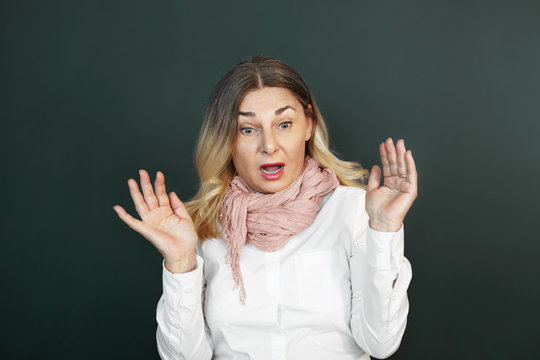 Portrait of emotional shocked senior woman with blonde loose hair looking in front of her with mouth wide opened, raising hands, feeling terrified and scared with spider or mouse. Fear and shock