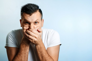Portrait of a man on a light background, covers his mouth with his hands, censorship, freedom of...