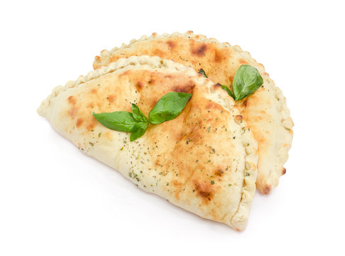 Two cooked calzone with basil twigs on a white background