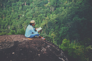 Asian man travel relax in the holiday. seats relax read books on rocky cliffs. On the Moutain. In Thailand
