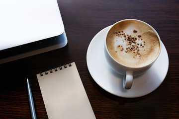 White coffee cup with notepaper and laptop on wooden desk table/nobody.lifestyle working and drinking concepts