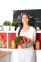 Smiling young woman holding vegetables standing in kitchen. Smiling young woman