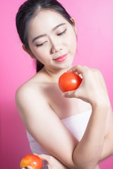 Asian woman with tomato concept. She smiling and holding tomato. Beauty face and natural makeup. Isolated over pink background.