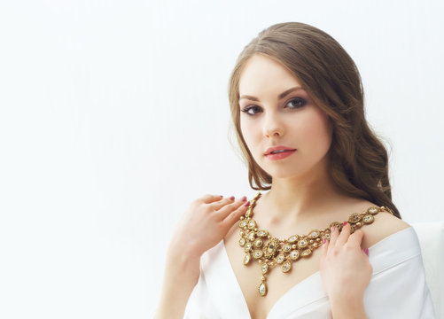 Beauty portrait of attractive and young woman trying golden necklace.