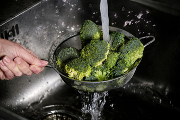 Woman's hand washing broccoli under running water at the kitchen sink. Lifestyle concept.