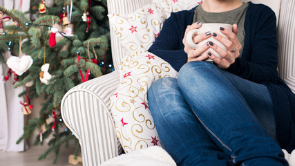 Young beautiful woman with short hair enjoying cup of tea, sitting in front of christmas tree. Authentic family xmas time