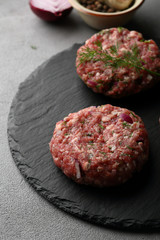 Raw minced meat cutlets on slate background