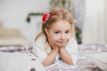 Happy little girl in a white sweater and blue jeans posing near christmas tree