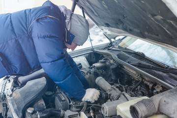A man in winter clothes on the street is engaged in repairing a car