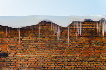 Icicles with snow hanging from a red brick wall