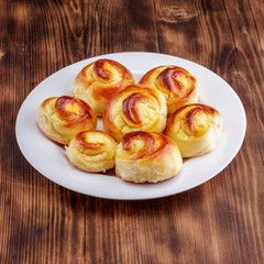 Twisted sweet buns with curd filling on a white plate on a wooden background