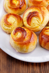 Twisted sweet buns with curd filling on a white plate on a wooden background
