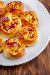 Twisted sweet buns with apple stuffing on a white plate on a wooden background