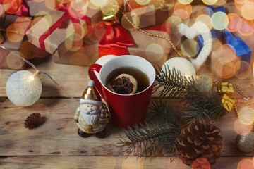 Image on a wooden background. Cup of tea, packed gifts, Santa Claus. Bokeh