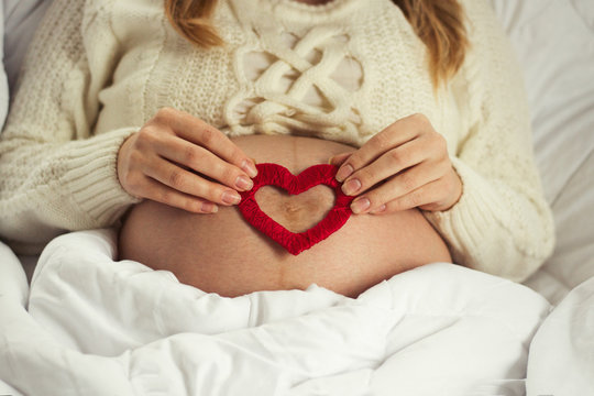 Pregnant young girl on her stomach holds the red heart of the handmade