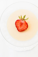 Creamy traditional Italian jelly dessert called Panna Cotta which is made of heavy cream, milk, vanilla and gelatin served in a cocktail glass and decorated with a strawberry on white table