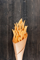 Potato fries with salt and pepper on the brown wooden background