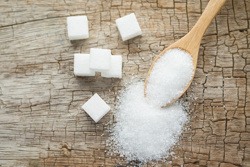 Bowl and scoop with white sand and lump sugar on wooden background