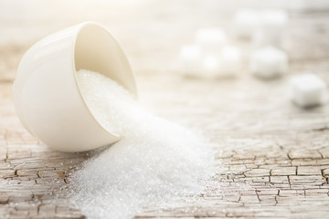 Bowl and scoop with white sand and lump sugar on wooden background