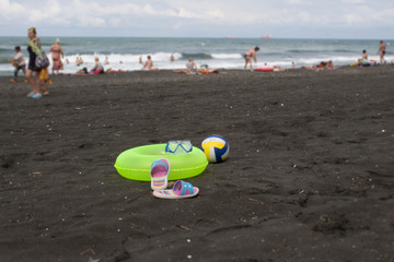 Ball, colorful sandal and yellow Floating Ring on beach. Blurred photo of people on sand beach. Travel or sea vacations concept