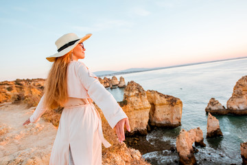 Woman enjoying great view on the rocky coastline during the sunrise in Lagos on the south of Portugal