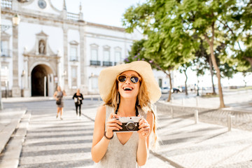Portrait of a young woman tourist standing with photo camera on the city gate background in Faro...