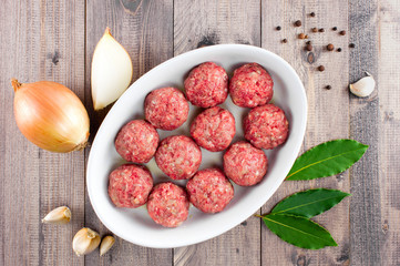 Raw fresh meatballs in the white plate on the wooden table