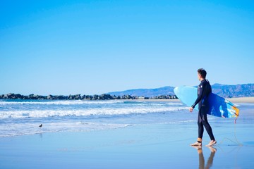 Male american surfer wearing full black wetsuit going to surf in Pacific ocean
