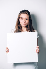 Naklejka premium young smiling woman holding a blank sheet of paper for advertising