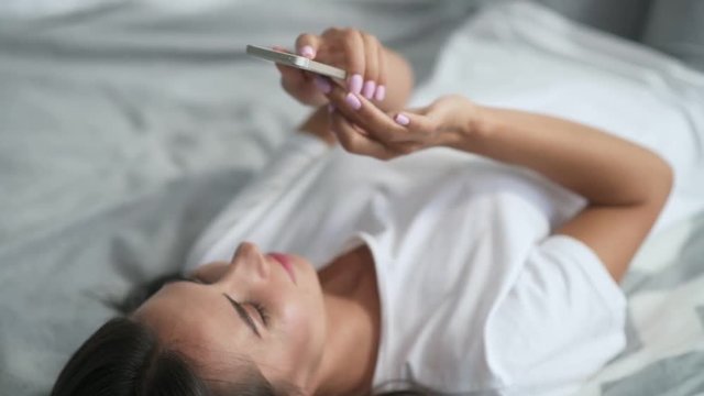 Set it off. Nice delighted young woman using her smart phone and lying in bed while enjoying her morning