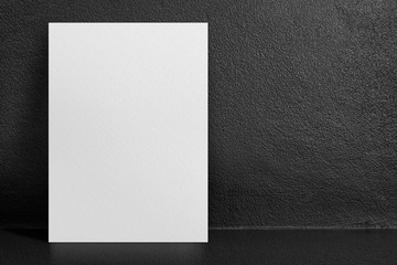 Blank white poster leaning at black interior cement room background,mock up template for display of...