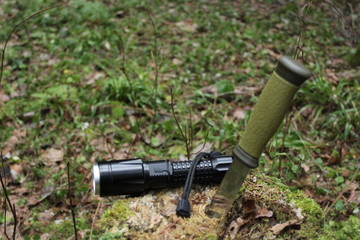 A green knife and a lantern on a stump covered with moss, against a background of green forest