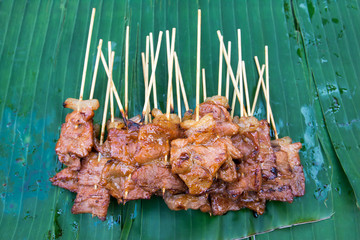 Grilled pork with bamboo sticks skewer on banana leaf background.Roast pork skewer with bamboo sticks