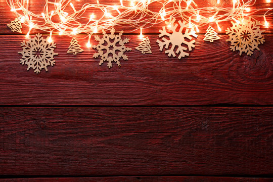 Picture of New Year's wooden red table with burning garland on top, snowflakes.