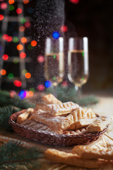 homemade cookies, glasses with champagne and a New Year tree on a festive table on a background of multi-colored New Year's lights