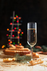 glass with champagne, biscuits, a Christmas tree and New Year's lights on a New Year's festive table