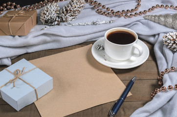 A cup of black coffee and gifts in a Christmas decor and a sheet of paper with a pen for text top view