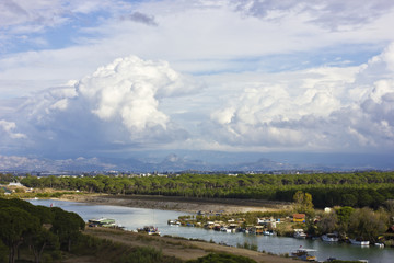 Landscape with a river and mountains. Large white cumulus clouds and purple clouds.