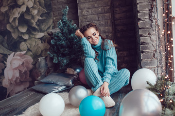Beautiful woman sits at home near window with christmas lights. New Year.