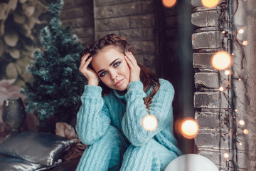 Beautiful woman sits at home near window with christmas lights. New Year.