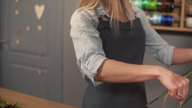 Side view of a flower shop assistant tying a bunch of flowers holding them in hands with the ribbon. Slowmotion shot