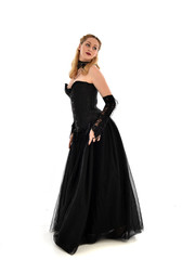 full length portrait of a blonde girl wearing black gothic gown. standing pose, isolated on white background.