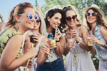 Group of girlfriends posing while drinking at outdoor party