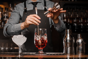 Barman making an alcoholic drink with ice in a cocktail glass